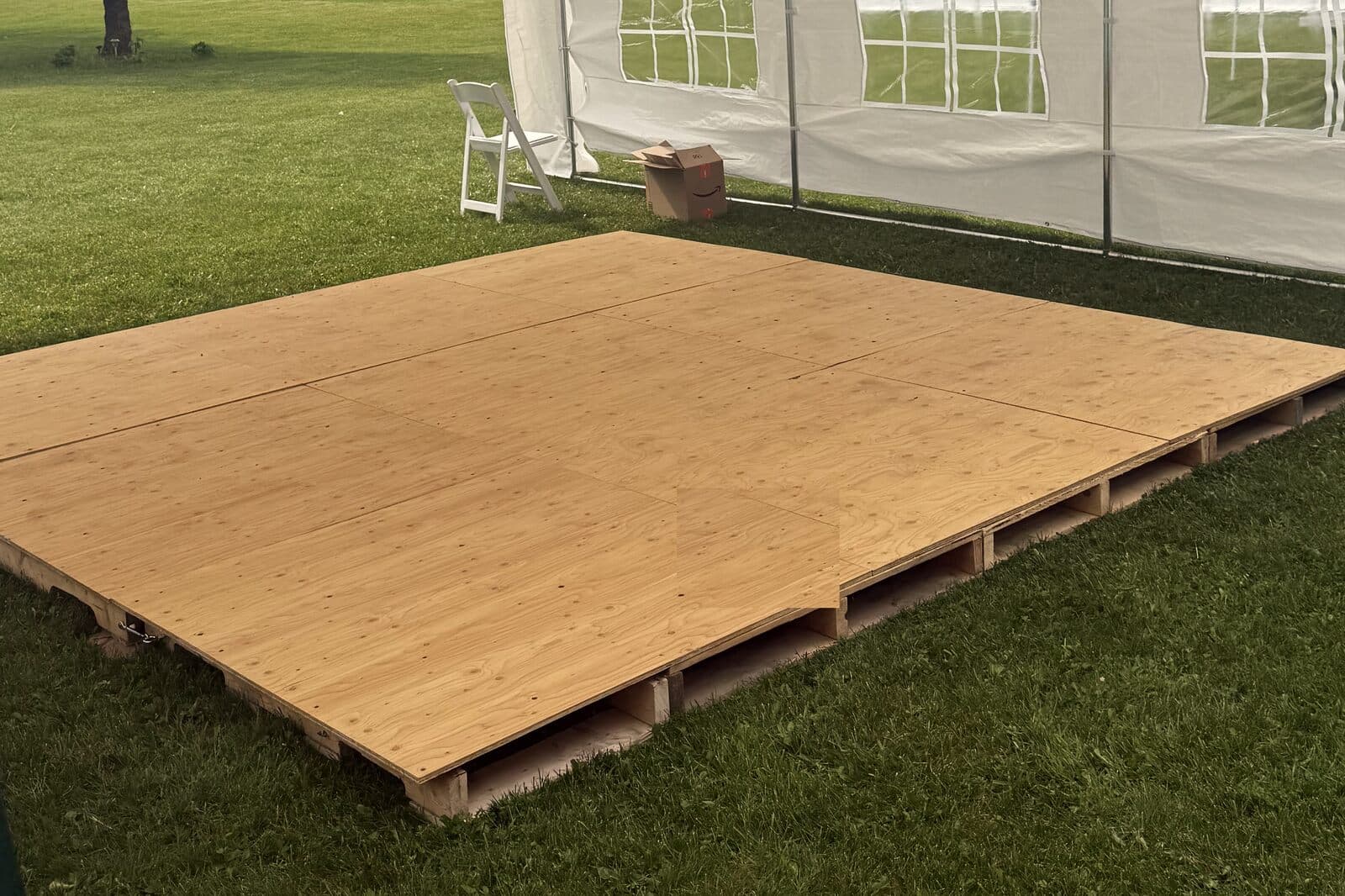 Wooden dance floor platform set on the lawn beside a white frame tent