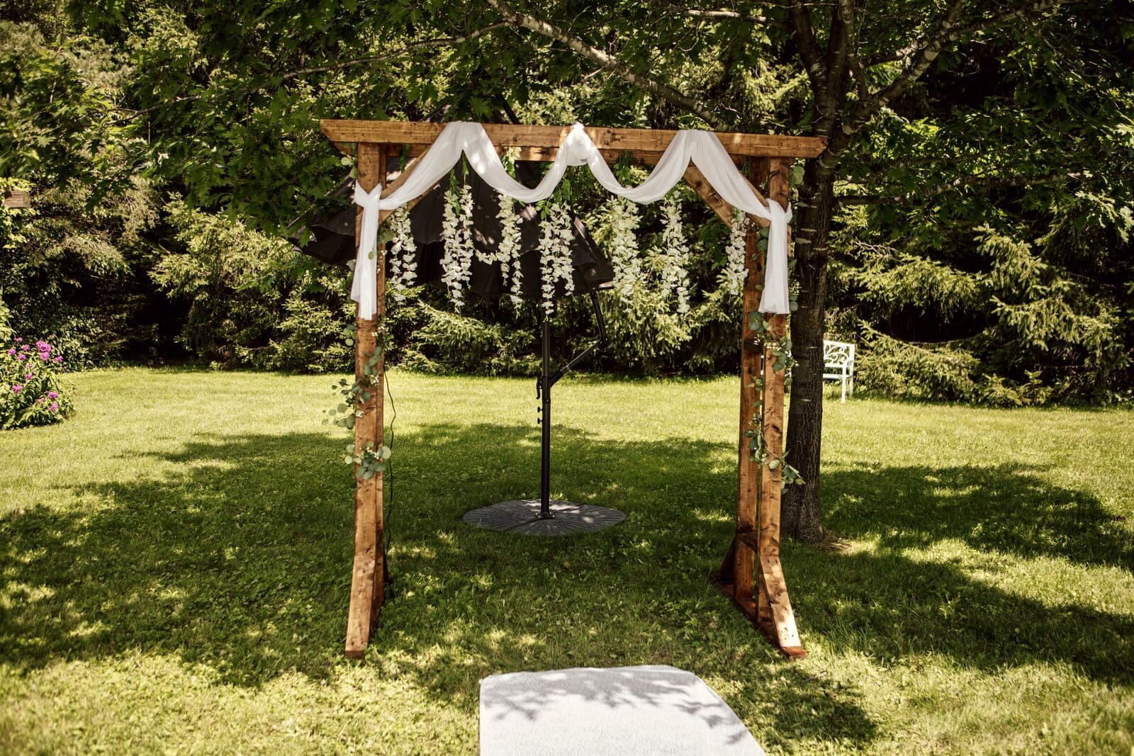 Birch-pole wedding arch with white draping and florals in the sun