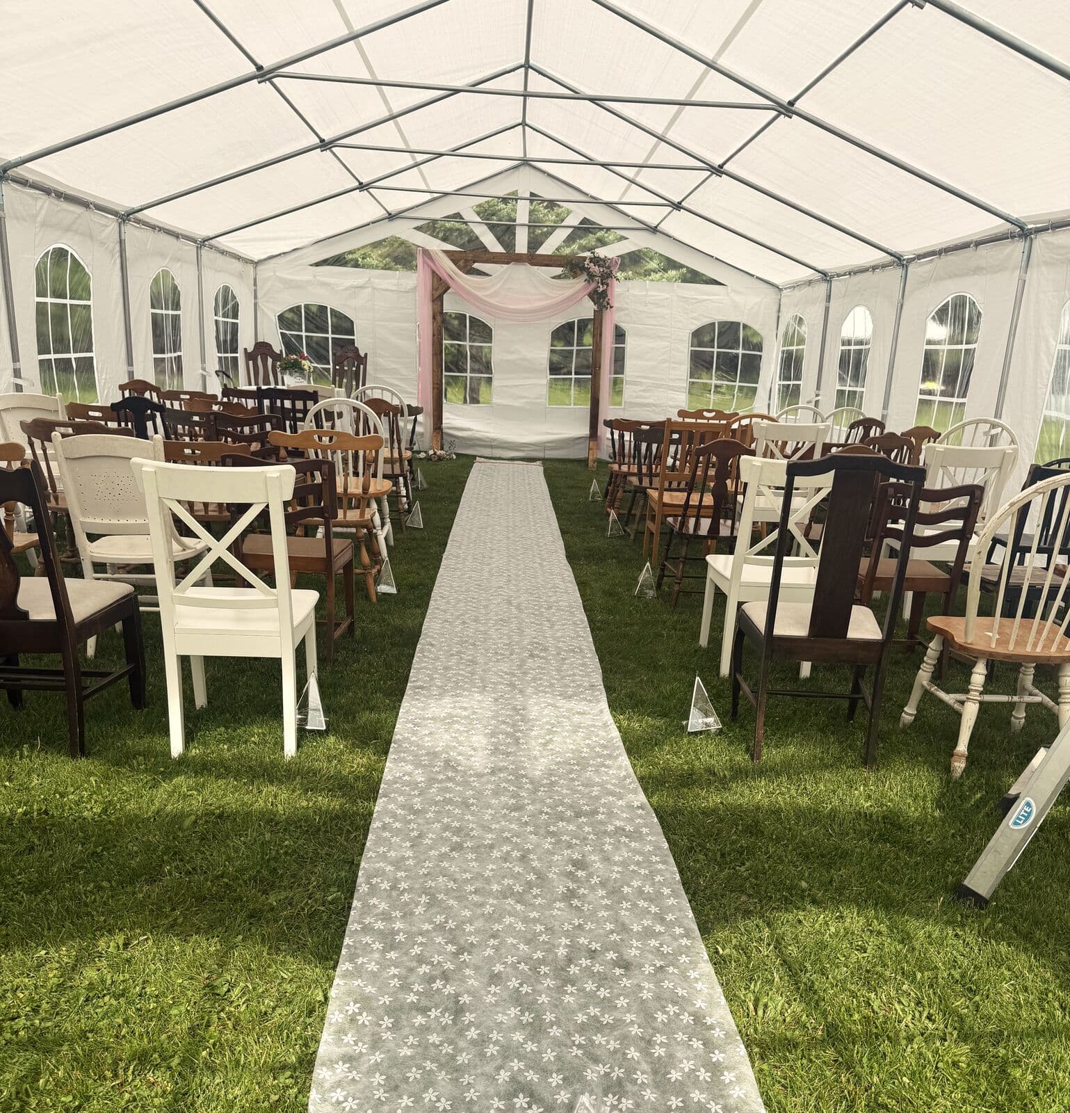 Lace aisle runner between rows of mismatched chairs, leading to the draped arch