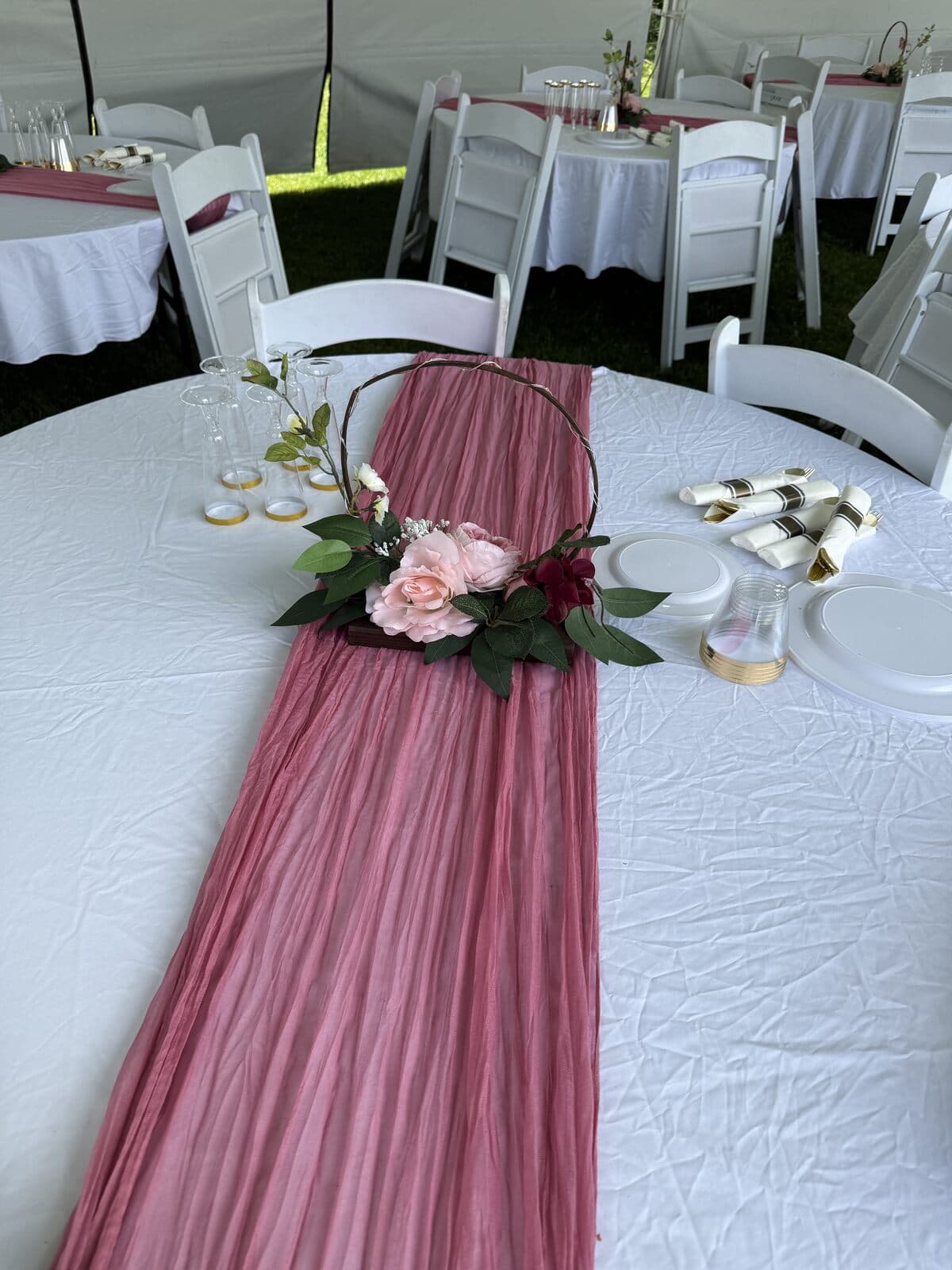 Round table with a rose runner and floral hoop centerpiece, dressed tables behind